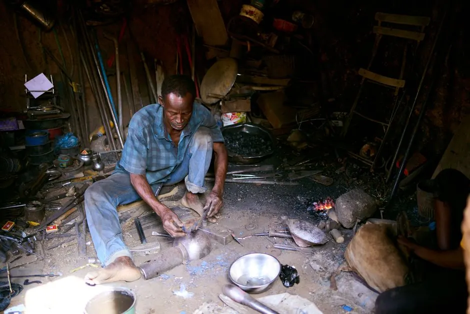 A blacksmith shaping metal with tools in a dimly lit, rustic workshop.